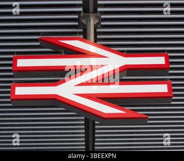 Close-up of a red and white railway logo sign in London. The sign is suspended from a ceiling structure. Stock Photo