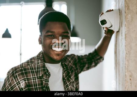 Smiling man installs security camera in modern office space during daytime Stock Photo