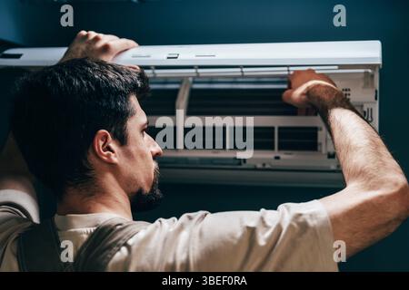 Technician performs maintenance on wall-mounted air conditioning unit in a modern room Stock Photo