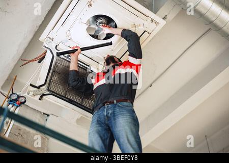 Technician repairs air conditioning unit in commercial building during afternoon Stock Photo