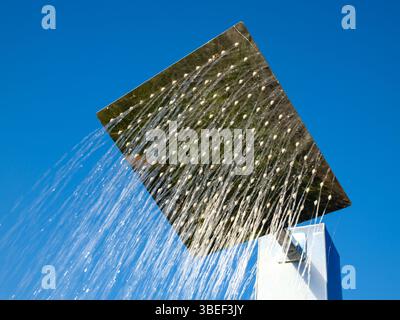 Large square rainfall showerhead with water cascading down against bright blue sky Stock Photo