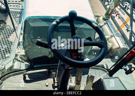 Close-up view of a modern tractor or telehandler cabin interior with steering wheel, control pedals, and industrial components, seen from the operator Stock Photo