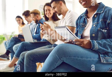 Cheerful multiracial young people in casual clothes sitting in row studying together indoors Stock Photo