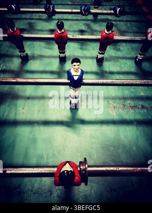 A lively table soccer game features diverse player figures in red, blue, and black, positioned on a green playing surface. Stock Photo