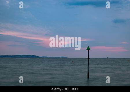 Green navigation pole in calm sea during dusk with pastel sky, Isle of Wight, UK. Symbol of maritime safety and coastal navigation. Stock Photo