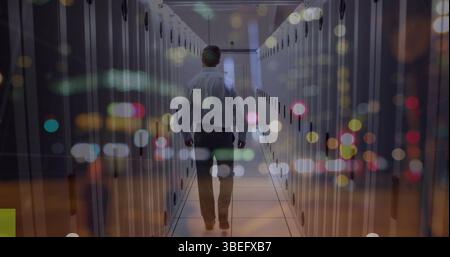 Walking IT technician wearing shirt navigating data center aisle with LED lights on server racks Stock Photo