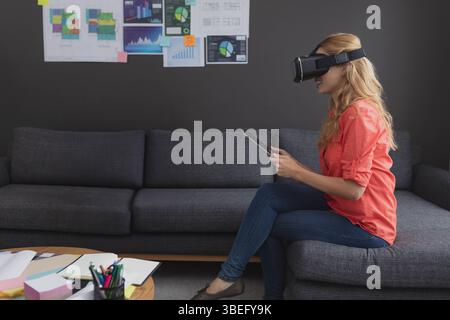 Virtual reality headset is resting on tablet on wooden coffee table, with scattered papers, charts Stock Photo
