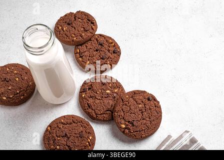 Chocolate cookies and bottle of milk on white background, top view, copy space. Homemade dark chocolate brownie cookies with hazelnuts. Stock Photo