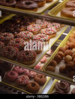 Sprinkles Covered Donuts on Display Rack Shelf at Bakery Shop Stock Photo