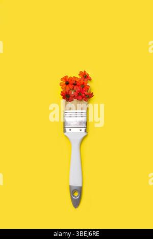 A white paintbrush with red flowers over the bristles on a yellow background with copy space Stock Photo