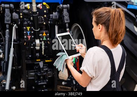 Female mechanic using digital tablet to manage farm equipment repair Stock Photo