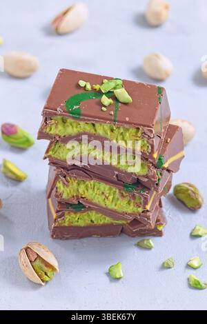 Milk chocolate bars with pistachio cream filling stacked on a table with whole and chopped pistachios, vertical Stock Photo