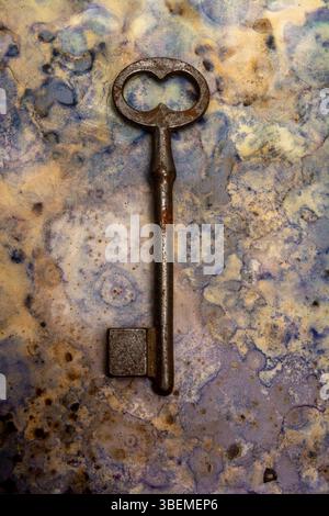 An old key lies against a blue and beige textured backdrop, showcasing its rust and wear. Stock Photo