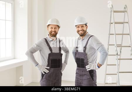 Two happy smiling construction workers wearing overall and safety helmet standing on building site Stock Photo