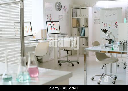 Contemporary laboratory setup with advanced equipment on white desks, featuring lab chairs, glassware, computers, and cabinets for storage and organiz Stock Photo