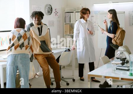 Group of colleagues engaging in discussion in bright, contemporary office space with various work materials visible Stock Photo