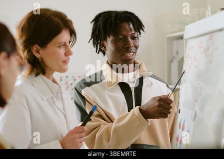 Teacher engaging students with chemistry lesson, holding lab equipment in science classroom. Multiracial participation in education visible Stock Photo