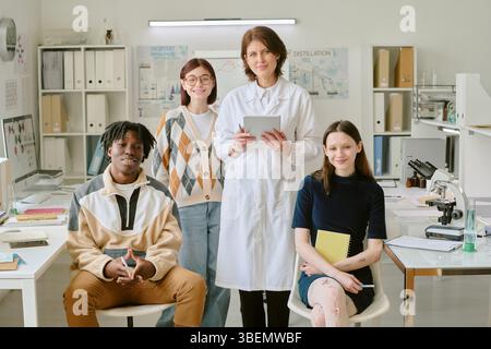 Diverse group of students collaborating on project in modern office environment, showcasing teamwork and engagement. Woman in lab coat holding tablet, Stock Photo