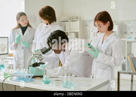Team of scientists working in modern laboratory, examining samples, and recording data. Diverse group wearing lab coats and safety goggles, surrounded Stock Photo