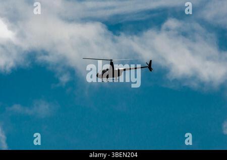 Centered view of a helicopter flying to the left in the clouds above a blue sky Stock Photo