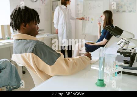 Scientists discussing test results and analysis in modern laboratory, showing teamwork and collaboration. Microscopes, test tubes, and charts visible Stock Photo