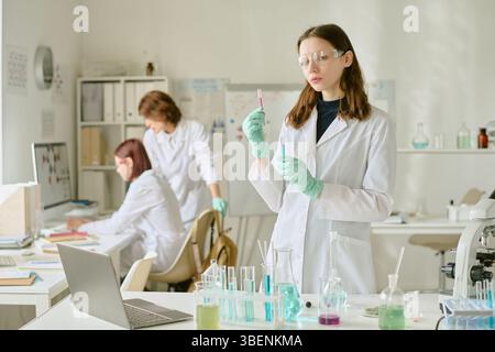 Scientists in lab coats conducting experiments with various chemical substances in modern laboratory environment having lab equipment and devices on b Stock Photo