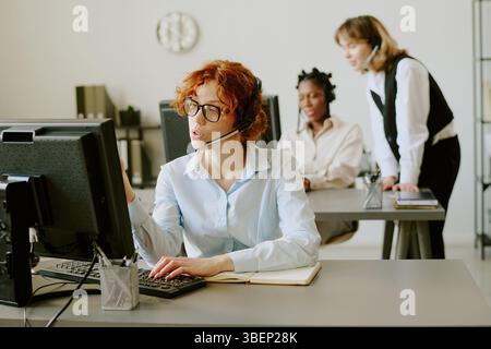 Diverse team working in office with headsets, collaborating and assisting clients by computer. Setting includes modern office furniture and open space Stock Photo