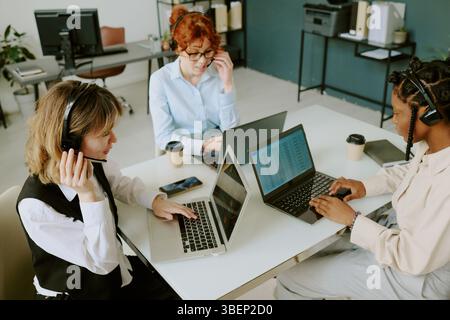 Group of diverse professionals working with laptops and headsets in modern minimalist office. Collaborating on projects in bright, airy environment wi Stock Photo