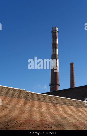Idustrial smokestacks behind weathered red and brown brick wall. Factory or plant chimney. Environmental impact and industrial emissions. Copy space Stock Photo