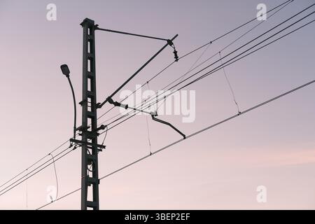 Overhead line equipment (OLE) used for railway electrification with catenary system and supporting pole. Infrastructure for trains, evening sky Stock Photo