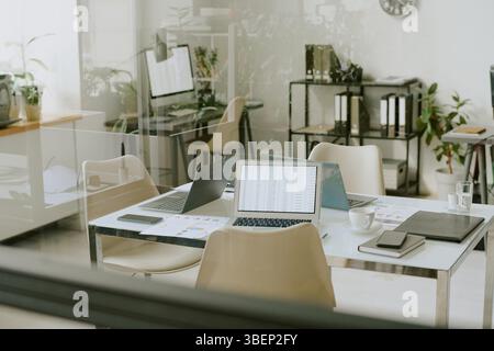 Contemporary office environment featuring open plan workstations with laptops and documents placed on desks under natural lighting conditions Stock Photo