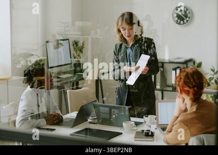 Group of diverse professionals discussing marketing strategy in modern office space with glass walls and modern decor. Business meeting focusing on pr Stock Photo