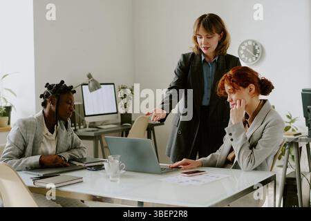 Multiracial business team engaging in strategic discussion in modern office. Group of professionals collaborating on laptop with documents and coffee Stock Photo