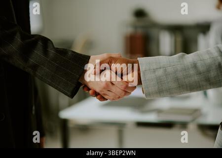Handshake between two professionals in formal business setting, symbolizing agreement and partnership. Office background with blurry objects in scene Stock Photo