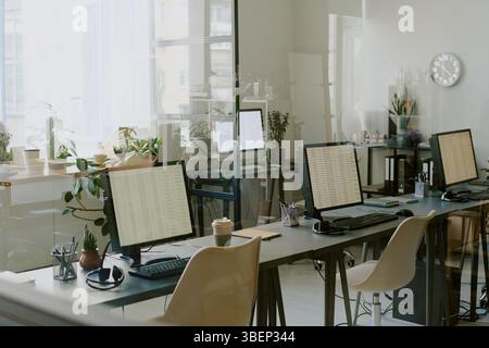 Empty office environment with several workstations set up, featuring computers, plants, and office supplies, reflecting clean and organized workspace Stock Photo