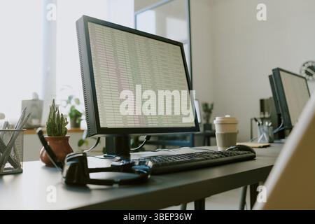 Office workspace featuring monitor displaying spreadsheet with coffee cup, keyboard, and headphones adding productivity tools to clean, modern desk se Stock Photo
