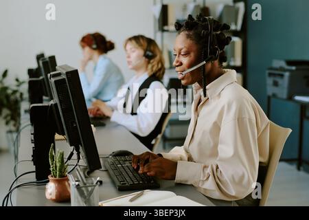 Woman wearing headset working in customer service call center with colleagues typing at computers in modern office environment Stock Photo