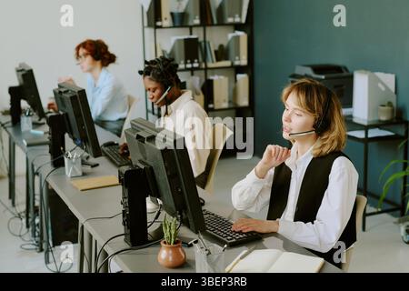 Diverse team working at call center with headsets, actively engaging with customers at modern workstations. Vibrant office ambiance with vocal interac Stock Photo