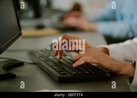 Focused hands on keyboard in modern office setting, with blurred background and technology present. Fingers actively engaged in typing Stock Photo