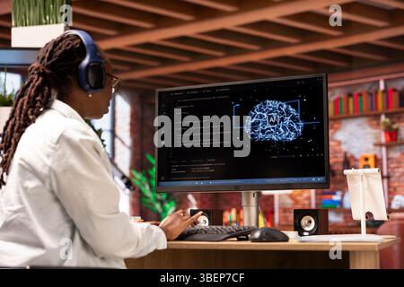 Freelancing computer engineer doing maintenance on artificial intelligence systems, listening music. Remote tech support specialist working from home wearing headphones, doing checkup on AI systems Stock Photo