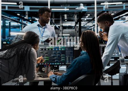 System administrators programming in AI data center housing advanced equipment used for machine learning training. Server hub employees run code on PC to upgrade artificial intelligence systems Stock Photo