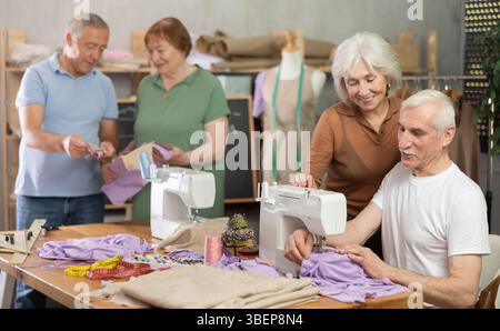 Some people communicate and discuss pattern, while others sew using sewing machine at lesson Stock Photo