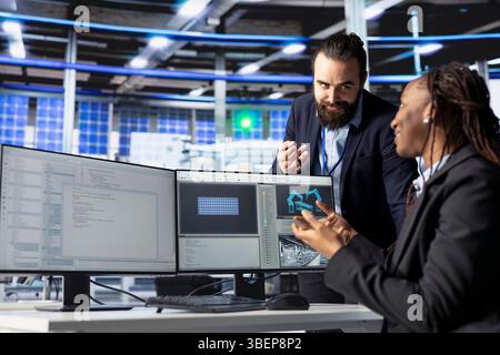Happy photovoltaics factory programmer building models of renewable energy generators, presenting progress to manager. Smiling solar panels plant developer building solar cells talking with supervisor Stock Photo