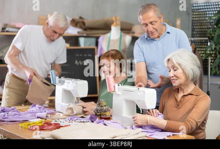 Some people communicate and discuss pattern, while others sew using sewing machine at lesson Stock Photo