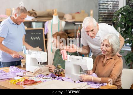 Some people communicate and discuss pattern, while others sew using sewing machine at lesson Stock Photo