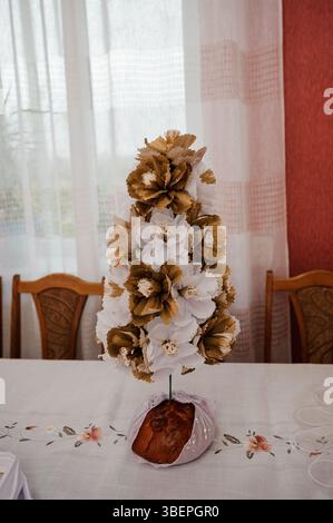 A meticulously crafted paper flower tower centerpiece in neutral and white tones stands on a table covered with a patterned tablecloth against a soft Stock Photo