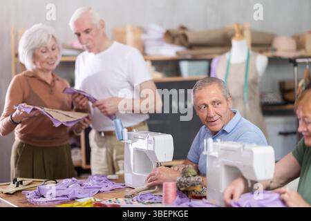Some people communicate and discuss pattern, while others sew using sewing machine at lesson Stock Photo