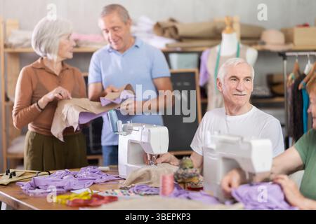 Some people communicate and discuss pattern, while others sew using sewing machine at lesson Stock Photo