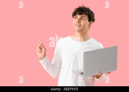Male programmer with laptop pointing at something on pink background Stock Photo