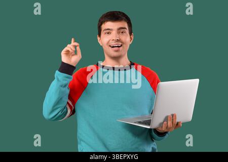 Male programmer with laptop pointing at something on green background Stock Photo